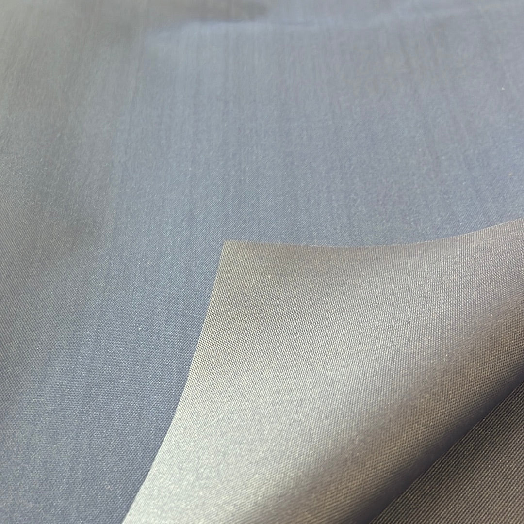 Close-up of solution-dyed polyester fabric in a muted blue tone, showing texture and drape.