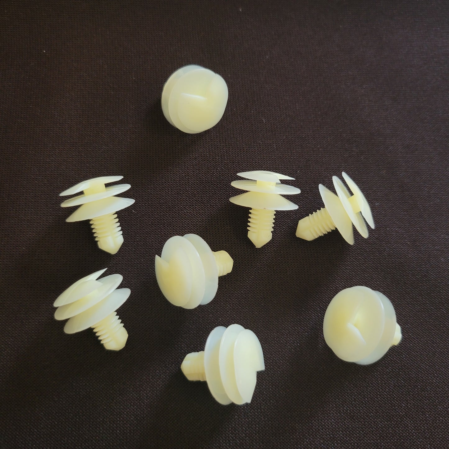 Off-white plastic car fasteners on brown fabric background