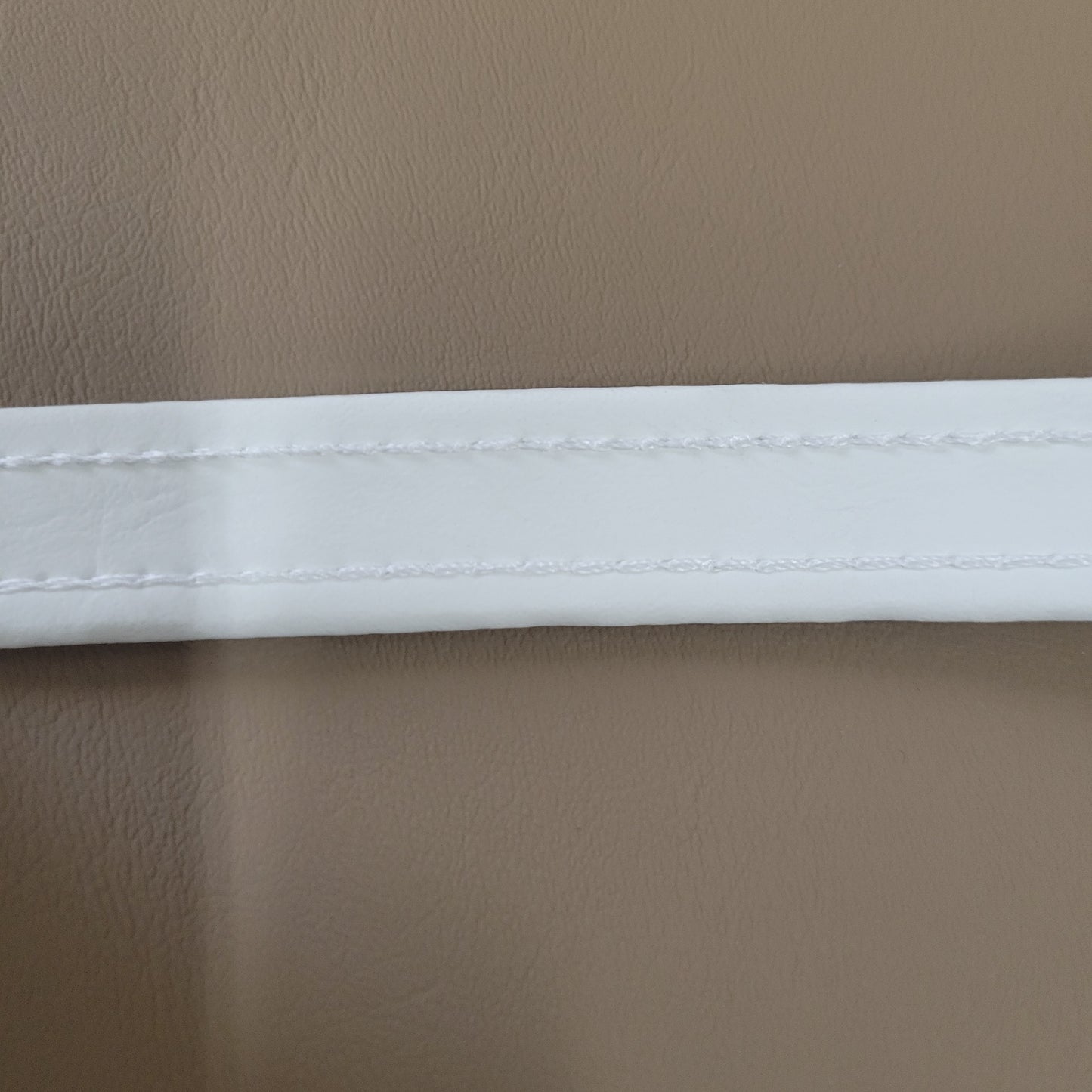 Close-up of white welt cord with stitching, shown against a taupe background.