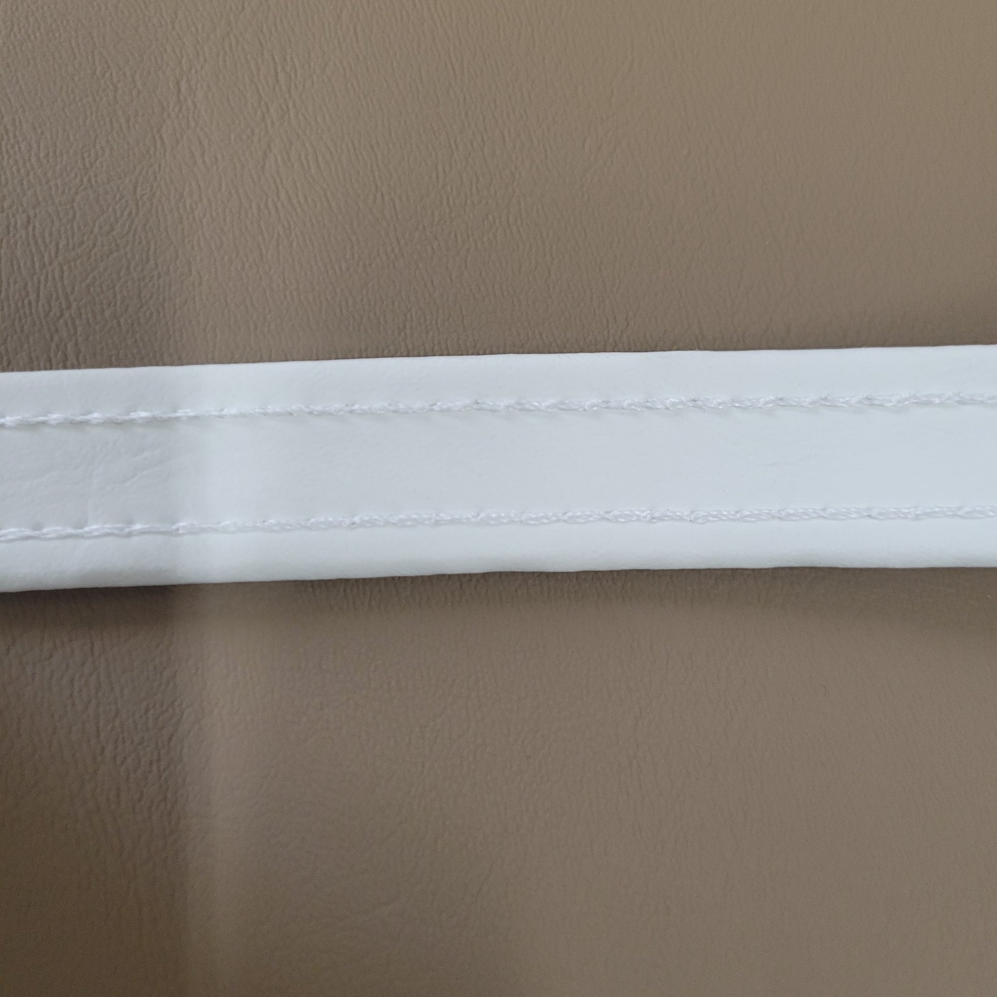 Close-up of white welt cord with stitching, shown against a taupe background.