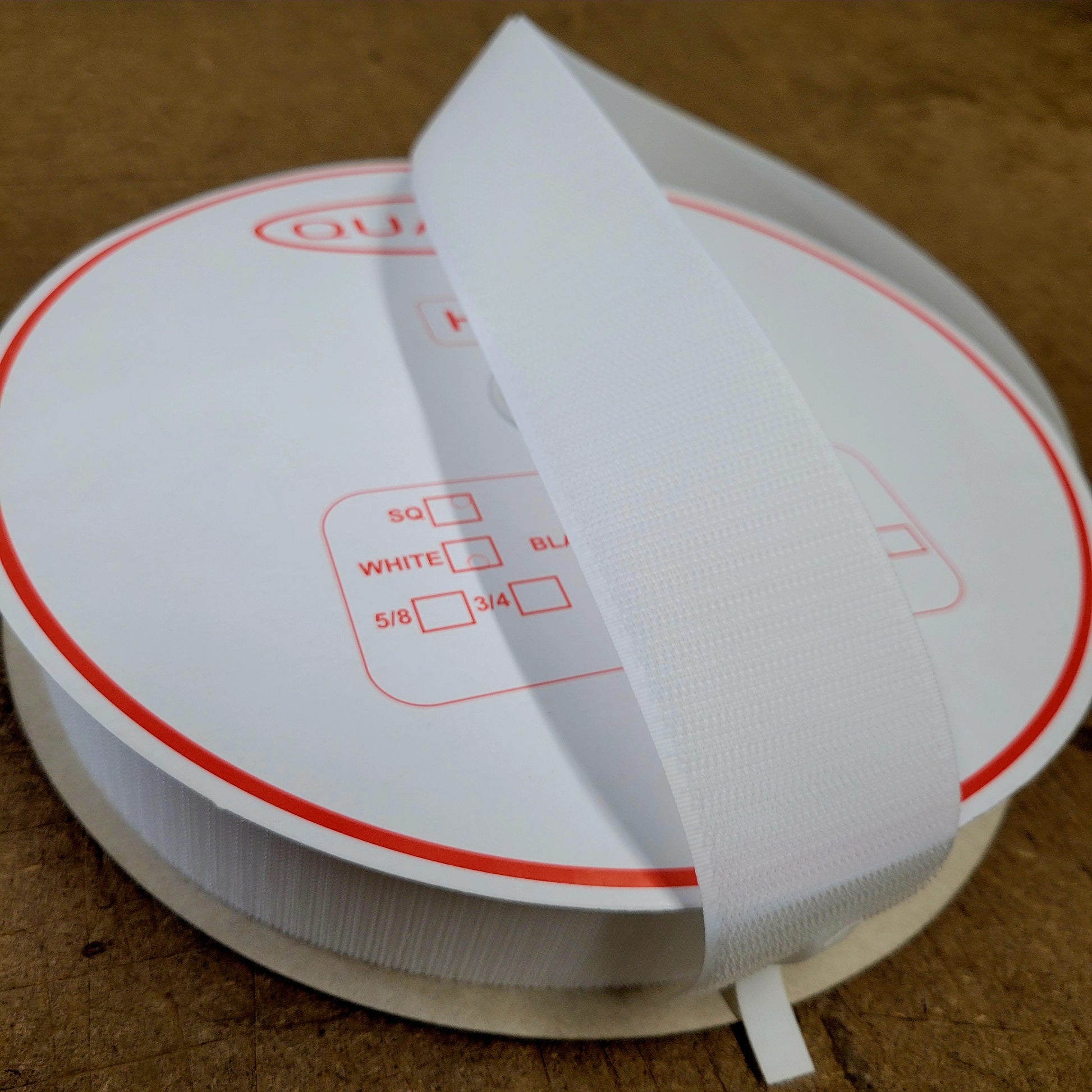 White sew-on hook and loop fastener, 25-yard roll shown on a wood surface.
