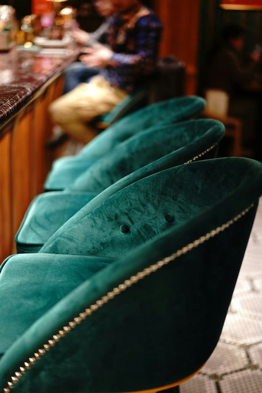 Row of green velvet upholstered chairs with brass nailhead trim along a bar